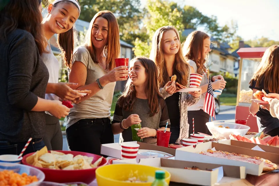 Group of people at table set ouf with picnic food on street during a neighborhood block party.